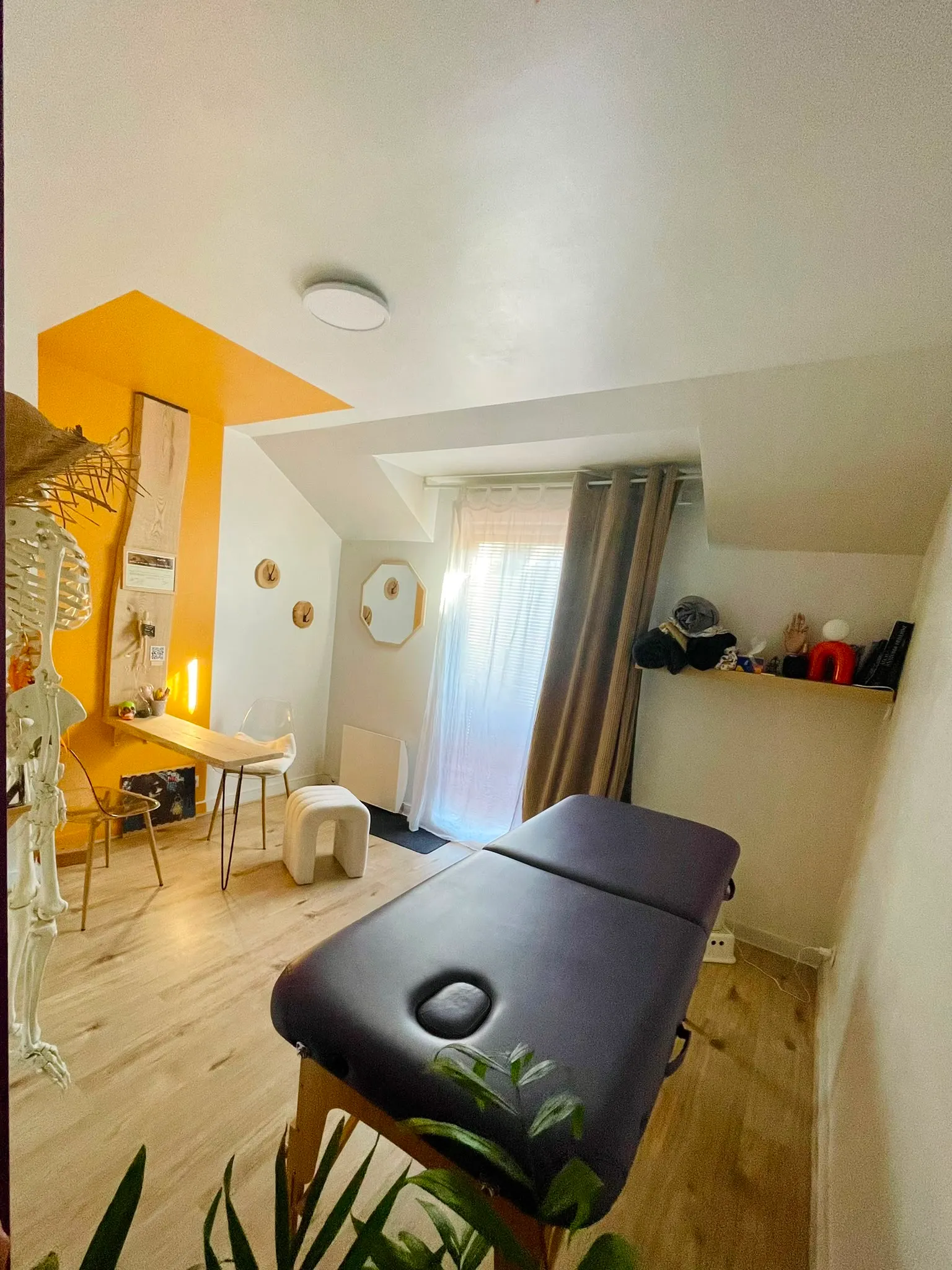 Salle de soin du cabinet : table de massage, lumière naturelle et espace d’accueil